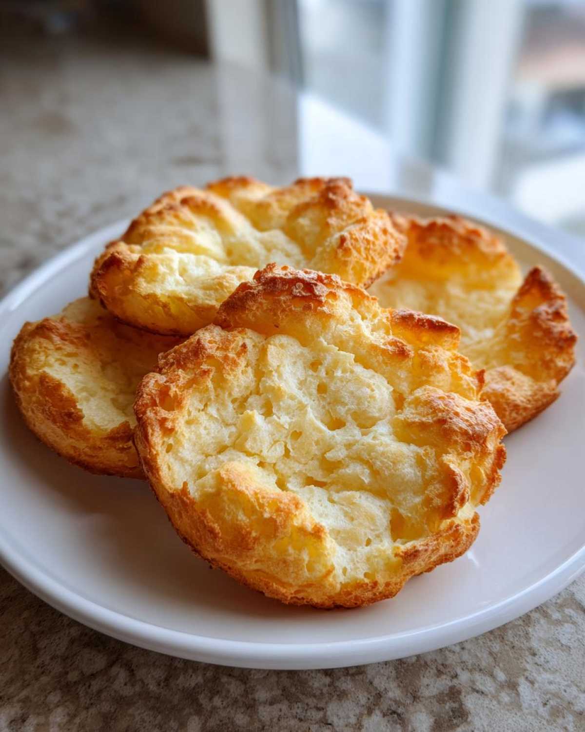 Four golden brown, fluffy pieces of cloud bread stacked slightly on a white plate.