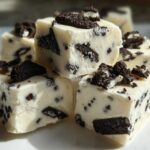 Close-up of creamy white Oreo fudge squares studded with dark cookie pieces, topped with crushed Oreo.
