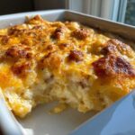 Close-up of a baked pierogi casserole in a white dish, featuring a golden, bubbly, cheesy topping.