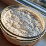 Close-up overhead shot of a very active sourdough starter, frothy and bubbly in a clear glass jar.