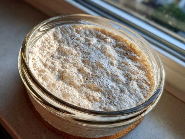 Close-up overhead shot of a very active sourdough starter, frothy and bubbly in a clear glass jar.