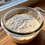 Close-up of an active, bubbly sourdough starter in a clear glass jar, showing signs of fermentation.