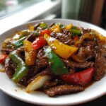 Close-up of a white bowl filled with glossy, saucy pepper steak strips mixed with colorful bell peppers and onions.