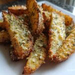 Close-up of golden brown, seasoned potato wedges topped with herbs and Parmesan cheese.