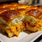 A close-up view of several baked buffalo chicken sliders filled with shredded orange chicken and melted cheese on a white platter.