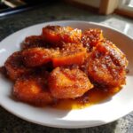 A white plate piled high with glistening, rich orange candied yams coated in a thick, sugary brown glaze.
