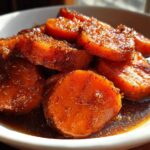Close-up of thick-cut, bright orange candied yams glistening in a rich, dark brown sugary glaze.