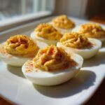 Close-up of perfectly piped deviled eggs garnished with paprika on a white platter.