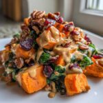 A close-up of a vibrant sweet potato salad featuring chunks of orange sweet potato, greens, dried cranberries, pecans, and a creamy dressing.
