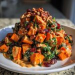 A mound of colorful sweet potato salad featuring roasted sweet potato cubes, kale, dried cranberries, pecans, and a creamy dressing.