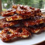 A close-up stack of crunchy pretzels coated in glossy, dark toffee and sprinkled with coarse salt, ready to eat.