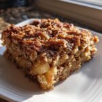 A square slice of apple cinnamon baked oatmeal topped with cinnamon sugar, served on a white plate.