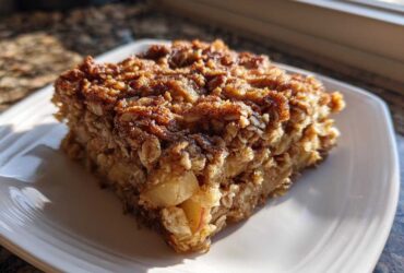 A square slice of apple cinnamon baked oatmeal topped with cinnamon sugar, served on a white plate.