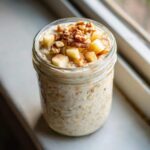A jar filled with creamy apple cinnamon overnight oats, topped with diced apples, walnuts, and cinnamon.