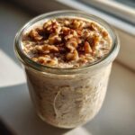 Close-up of apple cinnamon overnight oats in a glass jar topped with walnuts and cinnamon.