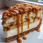 A decadent slice of apple pie cheesecake layered with apples and topped with crumble and caramel sauce.