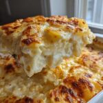 A spoonful lifted from a baking dish showing a thick, creamy slice of best scalloped potatoes recipe with a golden-brown top.