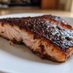 Close-up of a thick, moist fillet of blackened salmon with a dark, heavily seasoned crust on a white plate.
