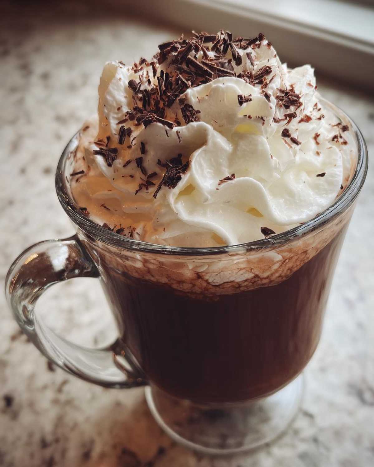 Close-up of a glass mug filled with rich boozy hot chocolate, topped with whipped cream and chocolate shavings.