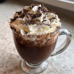 Close-up of a decadent boozy hot chocolate topped with a generous swirl of whipped cream and chocolate shavings.