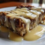 A close-up of a rich slice of bread pudding topped generously with creamy vanilla custard sauce.