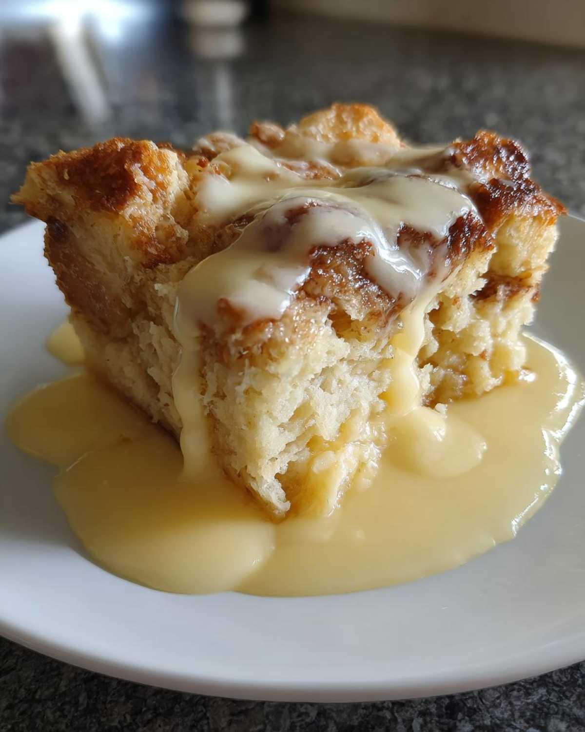 A close-up of a square serving of bread pudding recipe topped with thick vanilla sauce or custard.