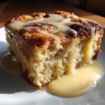 Close-up of a moist slice of bread pudding recipe topped with rich vanilla cream sauce.
