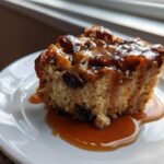 A close-up of a moist slice of bread pudding with bourbon sauce drizzled over raisins.