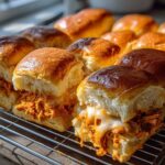 Close-up of freshly baked buffalo chicken sliders with gooey melted cheese oozing out, resting on a cooling rack.