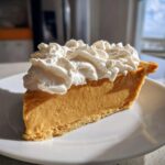 A thick slice of rich, creamy butterscotch pie topped generously with swirls of fresh whipped cream, sitting on a white plate.