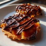 Two caramel ritz cracker christmas cookies topped with glossy caramel and drizzled with dark chocolate.