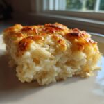A close-up of a square slice of creamy, cheesy potato casserole with a golden-brown, baked top.