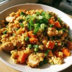 Close-up of a bowl of chicken cauliflower fried rice with carrots, peas, and green onion garnish.