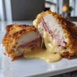 Cross-section of a crispy chicken cordon bleu showing melted cheese and ham oozing out.