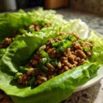 Close-up of savory chicken lettuce wraps filled with seasoned ground chicken, topped with fresh green onions and nuts.
