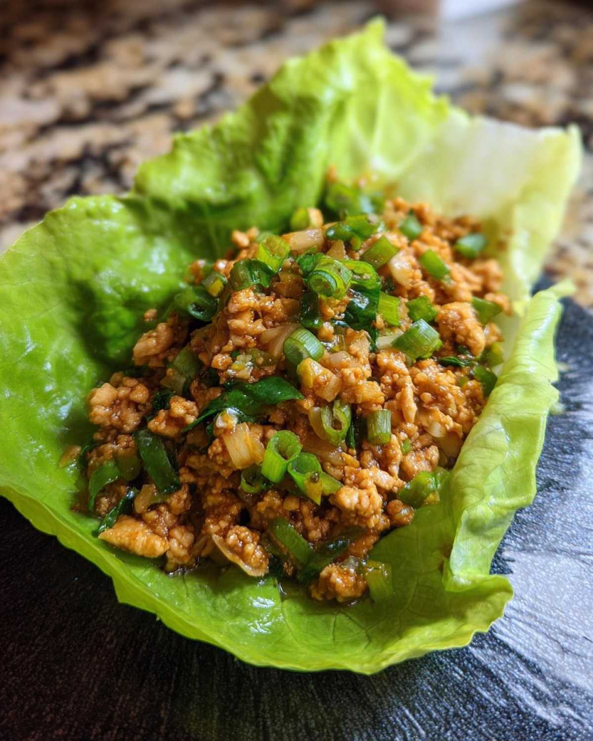 Close-up of savory seasoned ground chicken filling topped with green onions served in a crisp butter lettuce cup for chicken lettuce wraps.