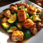 Close-up of glossy, saucy chicken zucchini stir fry pieces on a white plate.