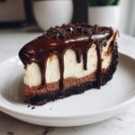 A decadent slice of chocolate cheesecake with a dark cookie crust, layered filling, and rich chocolate ganache dripping down the sides.