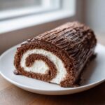 A cross-section of a delicious chocolate yule log cake showing the dark sponge rolled with white cream filling.