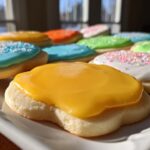 Close-up of sugar cookies decorated with bright, glossy sugar cookie icing in yellow, blue, green, and white with sprinkles.