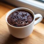 A rich, dark chocolate Cottage Cheese Microwave Brownie baked inside a white mug, topped with chocolate chips.