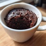 A rich, dark chocolate Cottage Cheese Microwave Brownie baked inside a white mug, topped with chocolate chips.