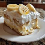 A generous slice of creamy banana pudding featuring layers of vanilla wafers, pudding, and whipped topping, garnished with fresh banana slices.