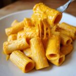 Close-up of rigatoni pasta coated in a thick, creamy orange butternut squash pasta sauce, with a fork lifting a piece.