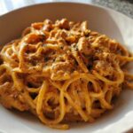 A close-up of creamy Cajun chicken pasta tossed with linguine or spaghetti noodles in a white bowl.