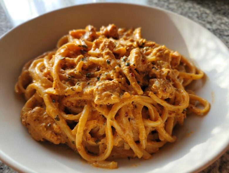 A close-up of creamy Cajun chicken pasta tossed with linguine or spaghetti noodles in a white bowl.