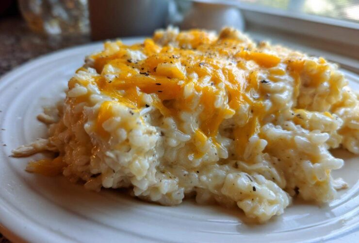 A close-up of creamy chicken and rice topped with melted orange cheddar cheese and black pepper.