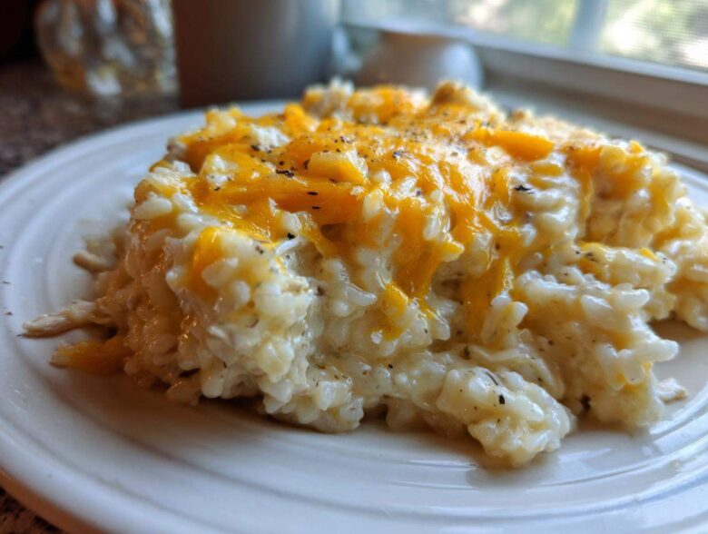 A close-up of creamy chicken and rice topped with melted orange cheddar cheese and black pepper.