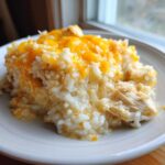 Close-up of a creamy portion of chicken and rice topped with melted cheddar cheese on a white plate.