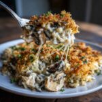 A spoonful of creamy chicken wild rice casserole showing melted cheese pulls and a crispy breadcrumb topping.